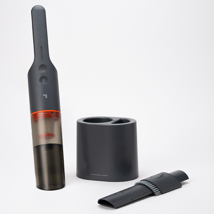 A sleek, modern handheld vacuum cleaner with a transparent dust compartment stands upright next to its matching black charging base and a separate nozzle attachment, all on a plain white background.